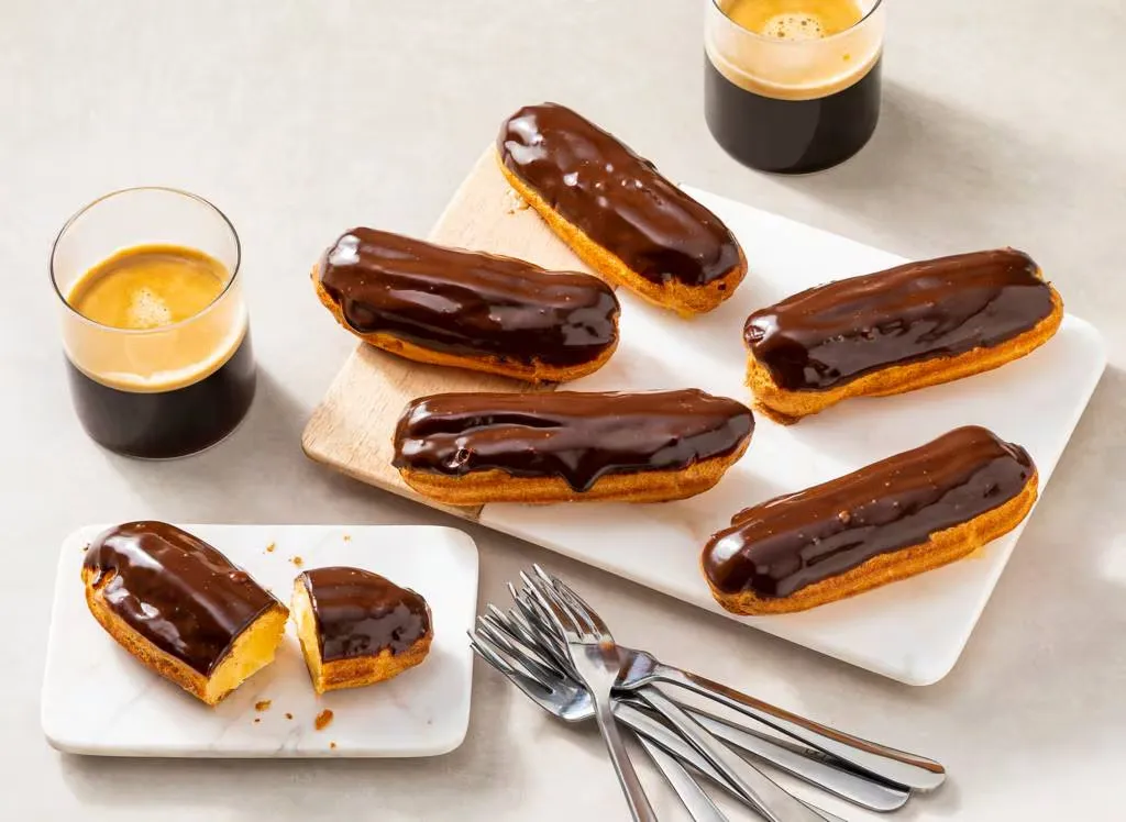 Rij verse eclairs met chocoladeglazuur en slagroom in een patisserievitrine